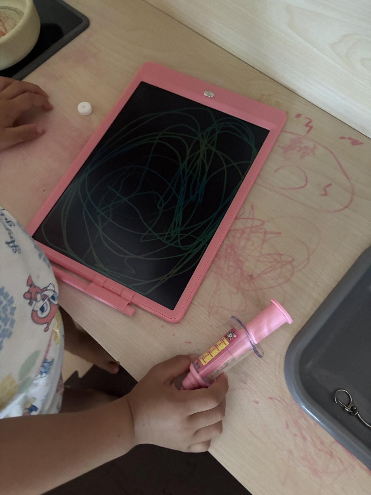 ピンクの電子メモパッドに落書きする子供の手と付属ペン