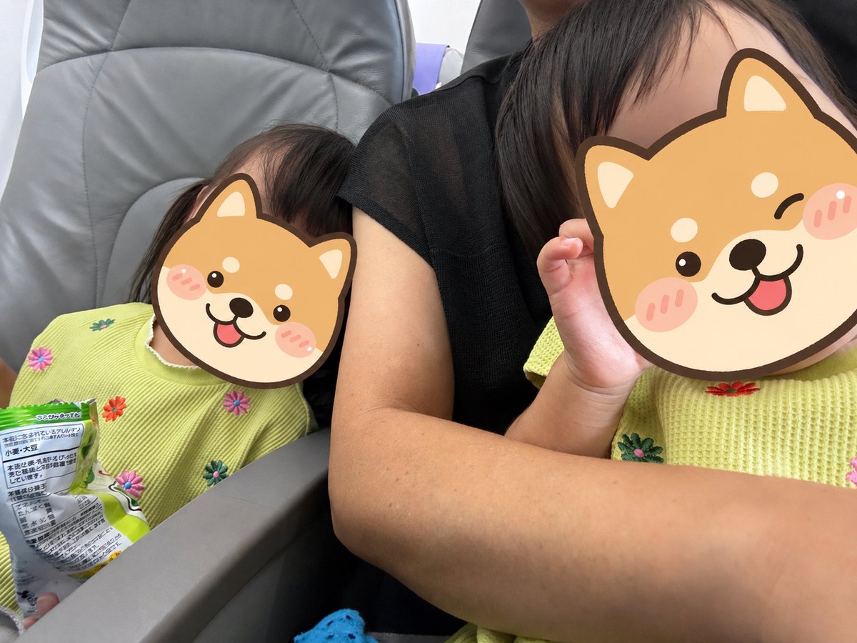 飛行機の座席でおやつを持つ3歳と1歳の姉妹
